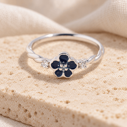 Sterling silver forget me not ashes ring with deep blue resin petals, clear sparkling accents and a twisting band, resting on cream stone.