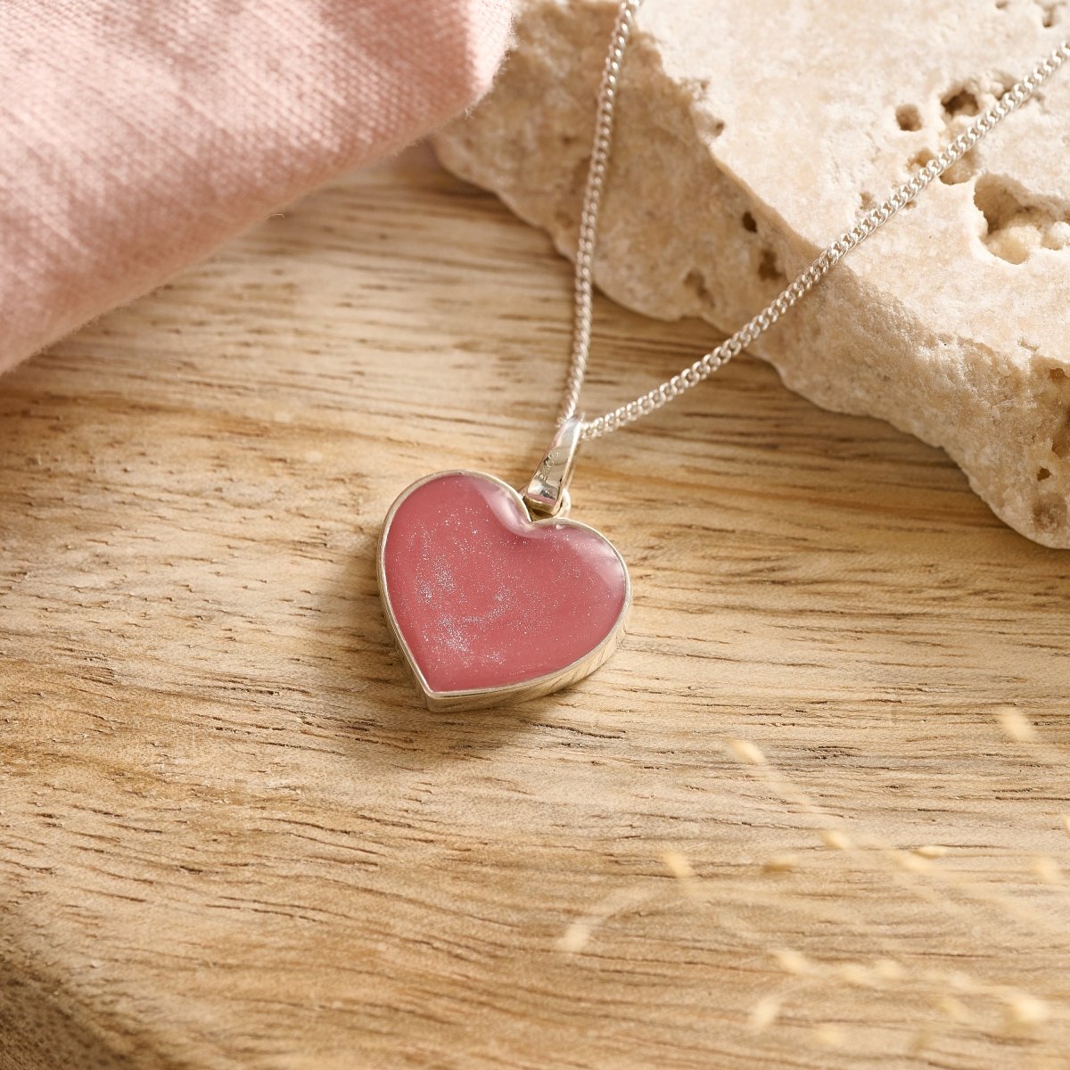 Close-up of sterling silver cremation necklace with pink resin on a wooden table.