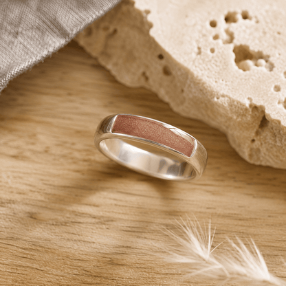 Silver mens ashes ring with brown resin inset for ashes, fur and hair on a wooden surface with a stone and feather.