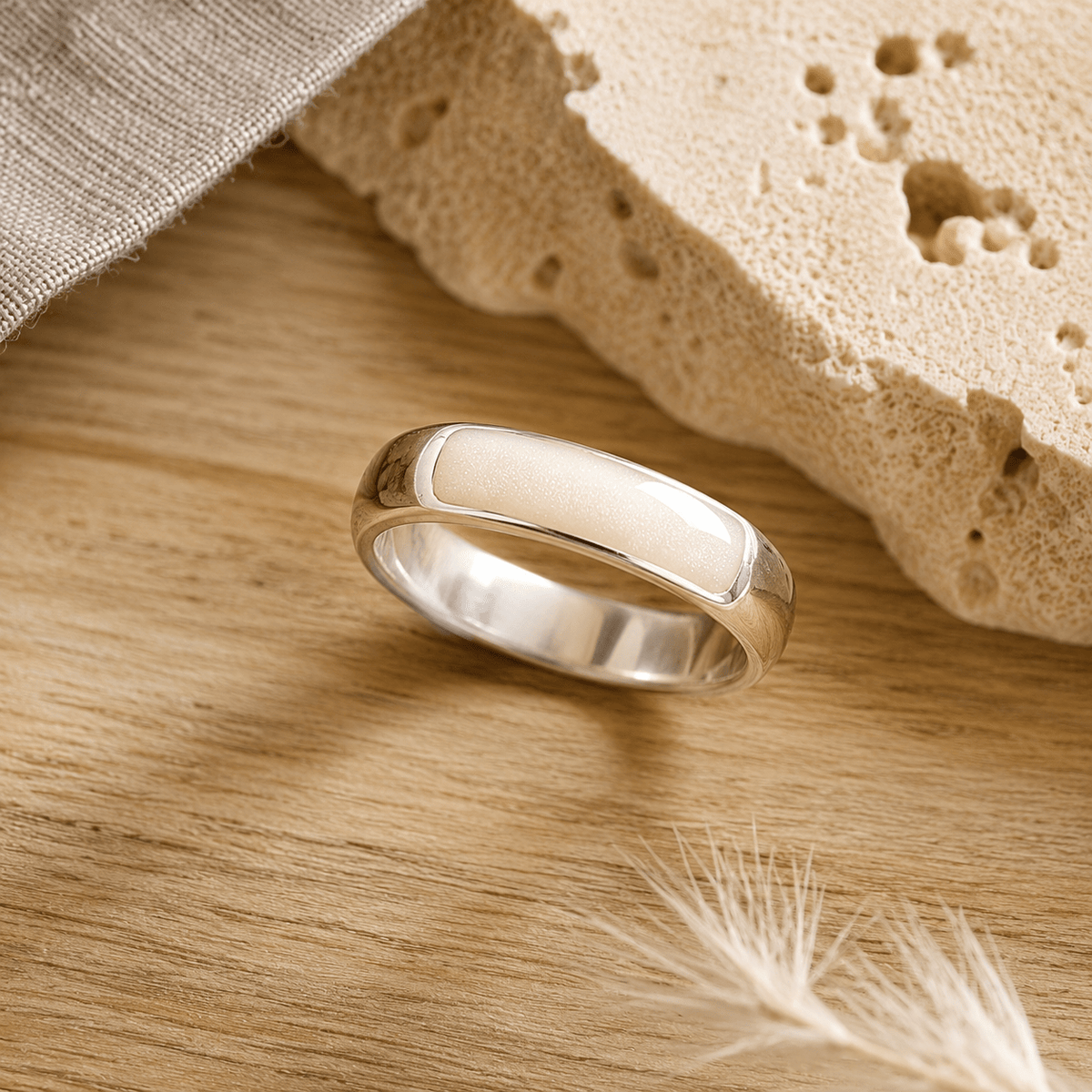 Silver mens ashes ring with white resin inset for ashes, fur and hair on a wooden surface with a stone and feather.