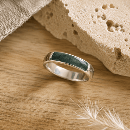 Silver mens ashes ring with evergreen resin inset for ashes, fur and hair on a wooden surface with a stone and feather.