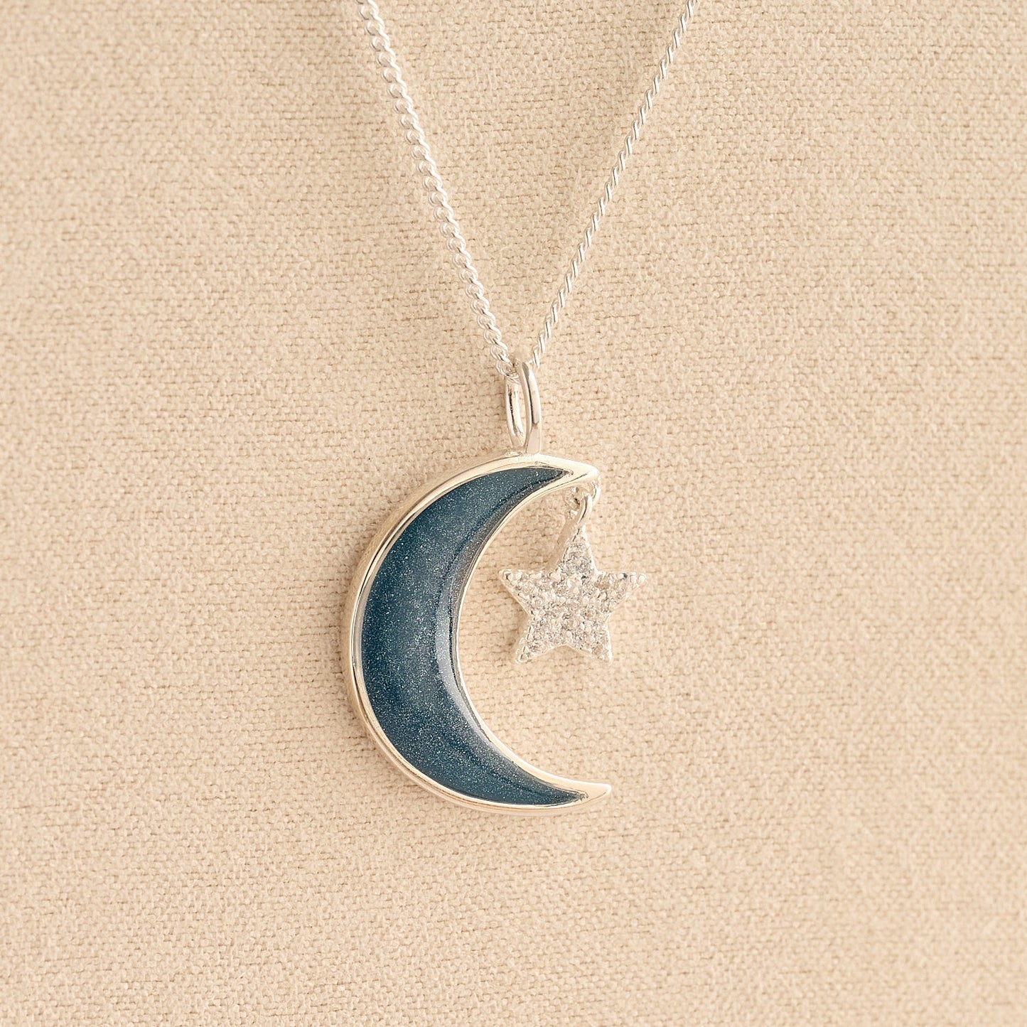 Moon and Star Ashes Necklace with navy resin filled with ashes or fur on a beige textured background