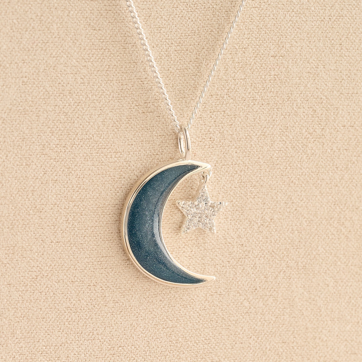Moon and Star Ashes Necklace with navy resin filled with ashes or fur on a beige textured background