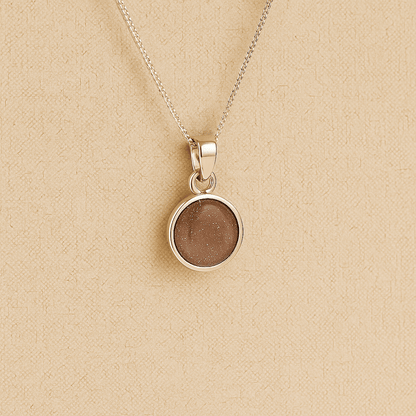 A round Silver Cremation ashes necklace mocha resin filled with ashes or fur, displayed on a soft beige background – suitable for pet or human memorials.