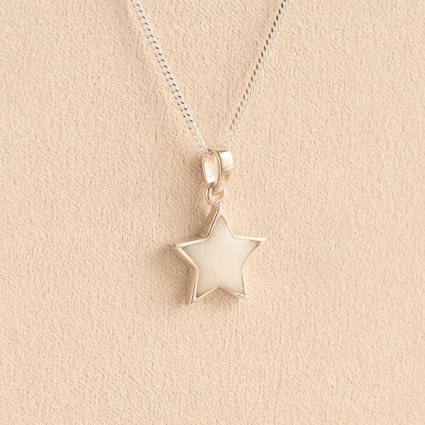 Silver star memorial pendant with white resin on a beige background