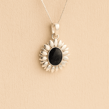 Silver Sunflower Memorial Necklace with a black resin infill containing ashes or fur set on a beige textured background