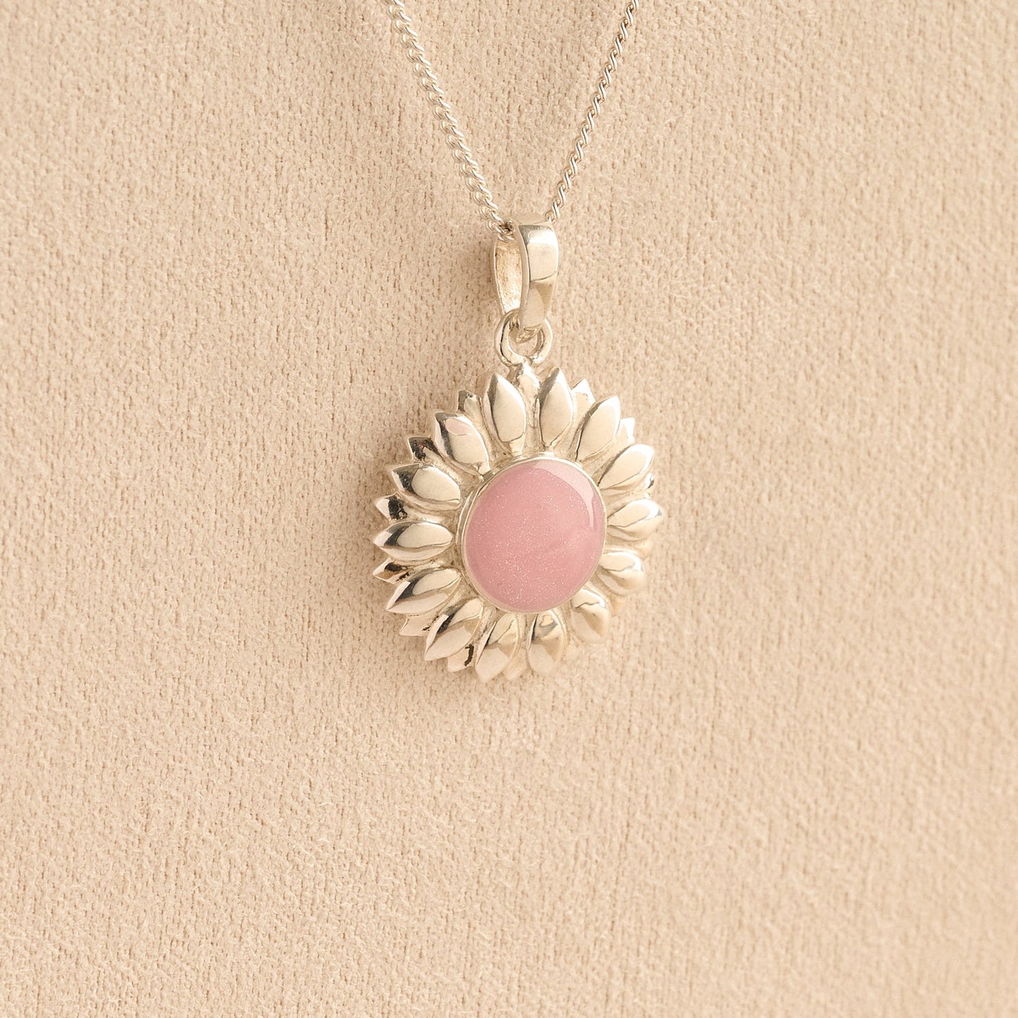 Sterling Silver Sunflower Ashes Necklace with a pink resin infill containing ashes or fur set on a beige textured background