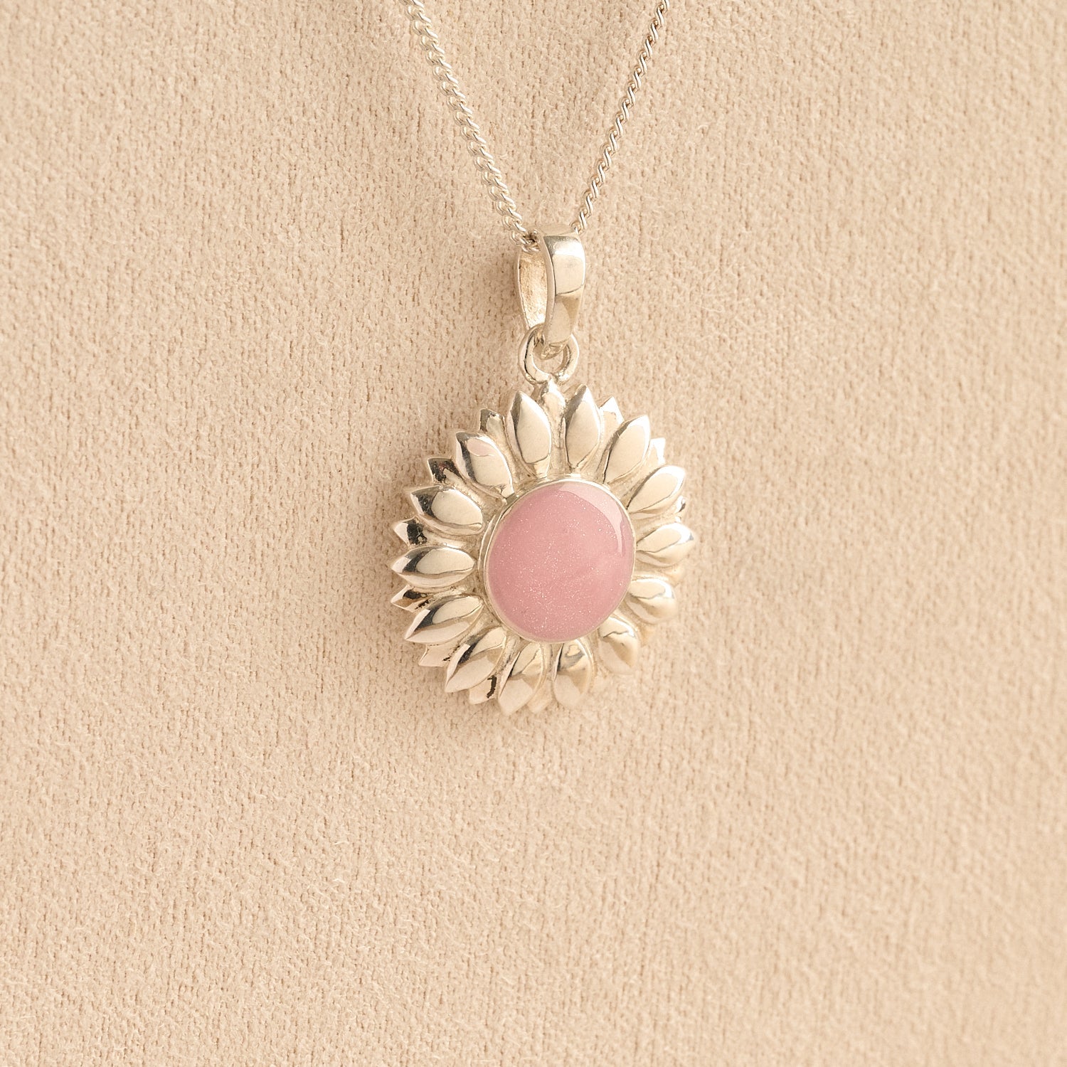 Sterling Silver Sunflower Ashes Necklace with a pink resin infill containing ashes or fur set on a beige textured background