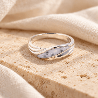 Sterling silver wave ashes ring with flowing polished curves around a pearly white resin setting containing visible ashes, resting on cream stone.
