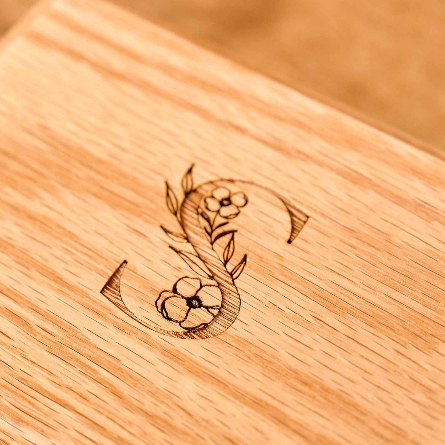 A close up of an engraving on a personalised cremation urn. The letter S is shown with a floral design. Personalised urn.