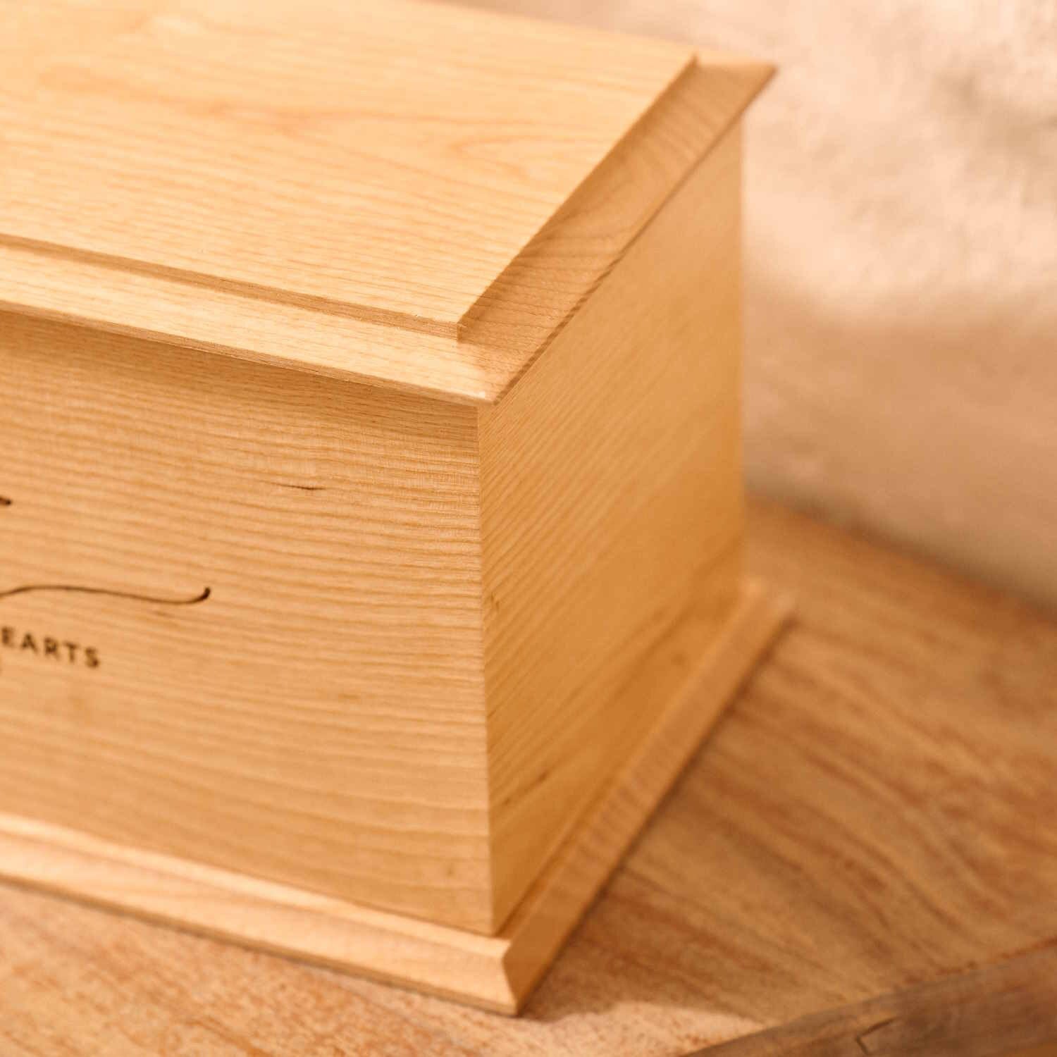 Close-up of engraved ash wood cremation urn with laurel wreath design – detailed view of custom memorial