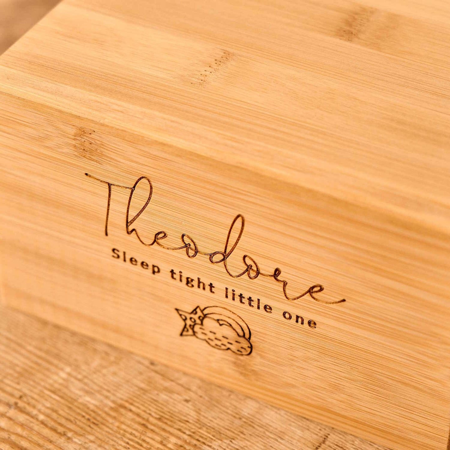 A small cremation urn for a stillborn baby or a miscarriage sits on a table. It is engraved with a cloud and rainbow motif and the name "theodore". A message reads "sleep tight little one". It is a personalised cremation urn.